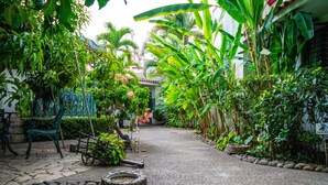A garden pathway with a stone bench, a small fountain, and lush tropical plants.