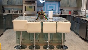 A modern kitchen with a central island, bar stools, stainless steel appliances, and a tiled backsplash. - Totally Renovated  with Amazing Kitchen, Luxurious Master Suie and Private Pool  (Lake Charles)