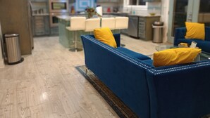 A modern living room with a blue sofa and yellow pillows, a glass coffee table, and a kitchen in the background. - Totally Renovated  with Amazing Kitchen, Luxurious Master Suie and Private Pool  (Lake Charles)
