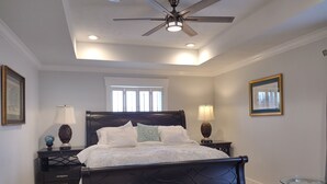 A bedroom with a dark wooden bed, two bedside tables with lamps, a ceiling fan, and a large window. - Totally Renovated  with Amazing Kitchen, Luxurious Master Suie and Private Pool  (Lake Charles)