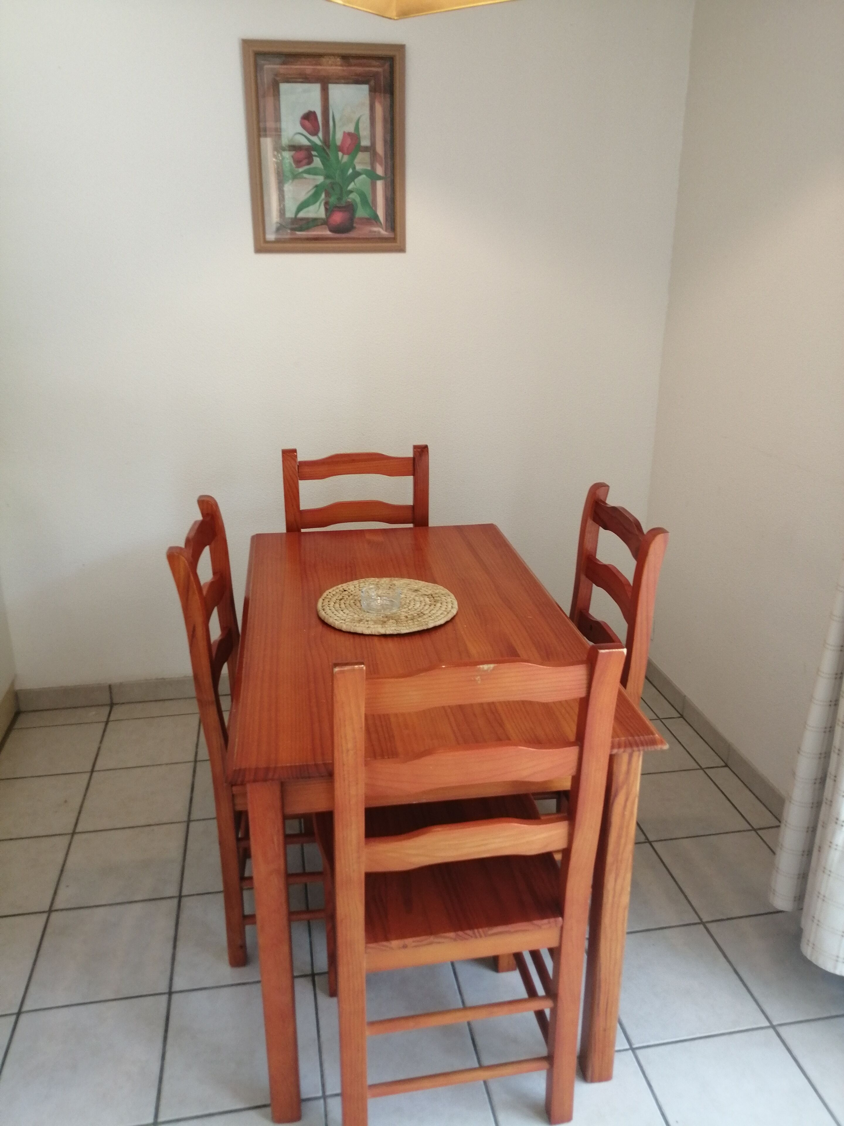 Une table à manger en bois, avec six chaises, un set de table en fibres tressées et un tableau encadré représentant des fleurs, accroché au mur.