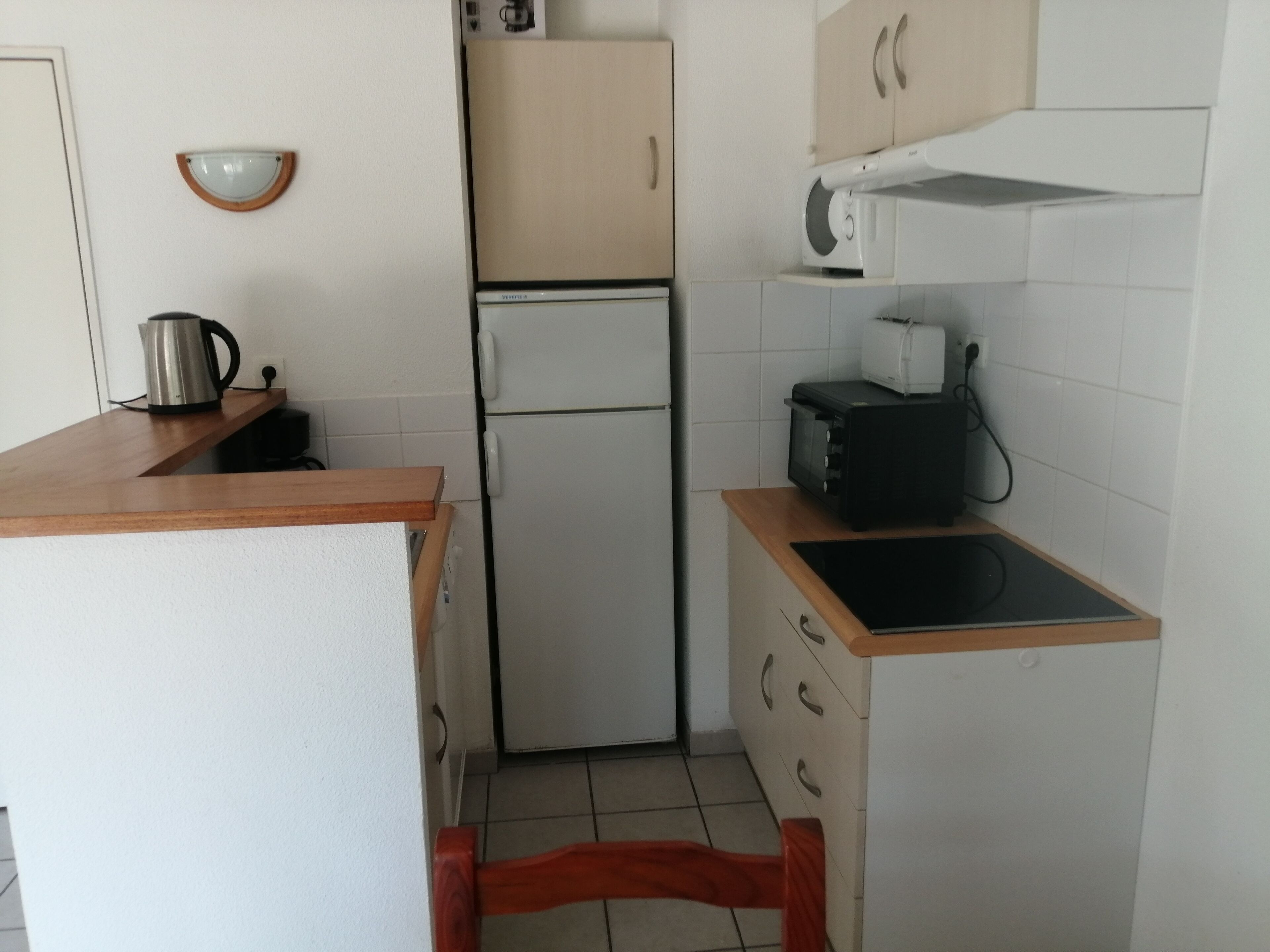 A compact kitchen with a refrigerator, microwave, toaster, and a kettle on the countertop.