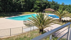 A swimming pool with a curved edge, surrounded by a fence and palm trees. - Appartement à la mer (Soulac-sur-Mer)