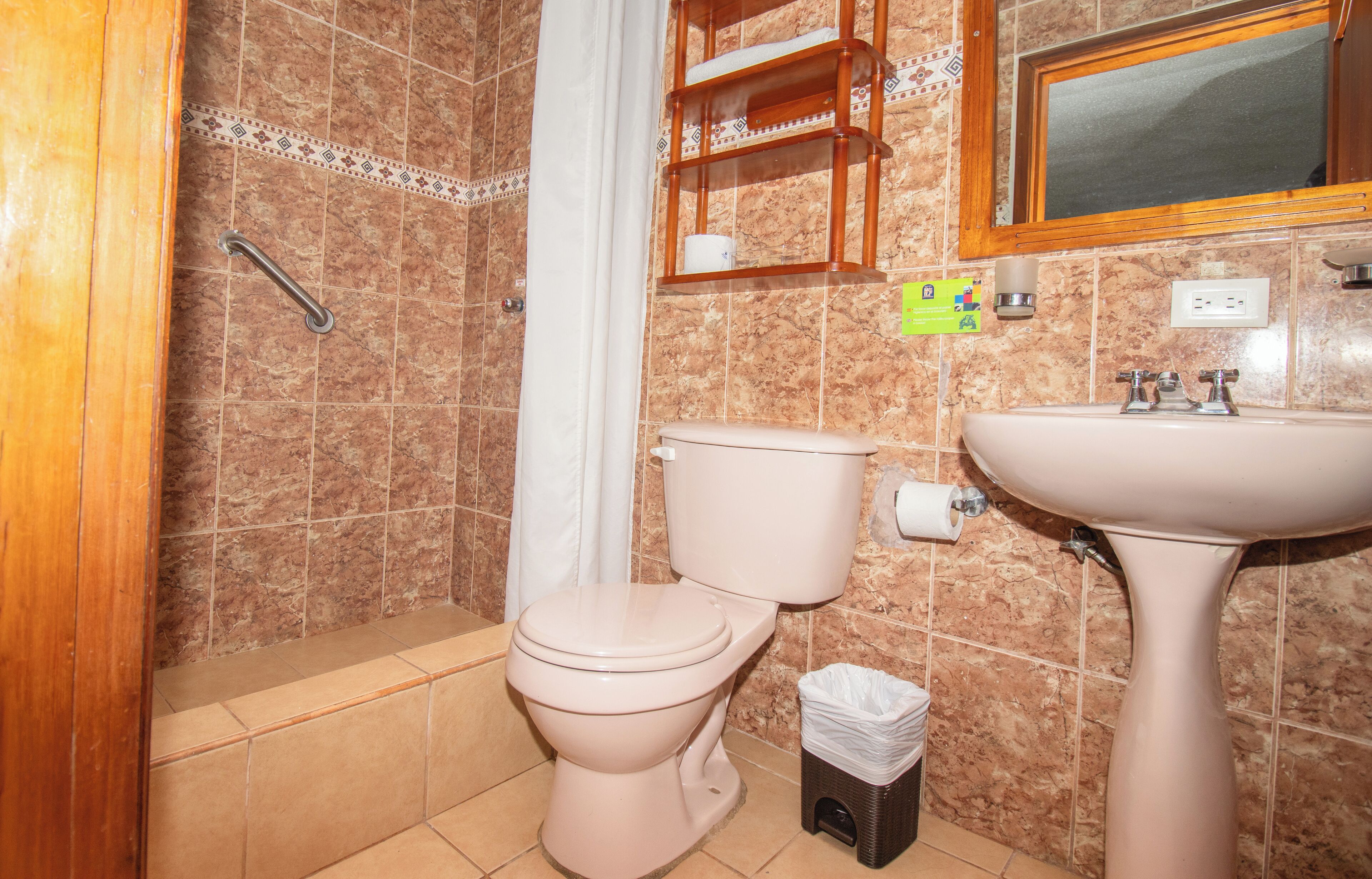 Un baño con inodoro, lavamanos, cortina de ducha y un cubo de basura pequeño.
