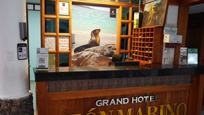 A reception desk at the Grand Hotel Leon Marino with a sea lion statue, wooden paneling, and various informational signs. - Grand Hotel Leon Marino Galapagos (Puerto Ayora)