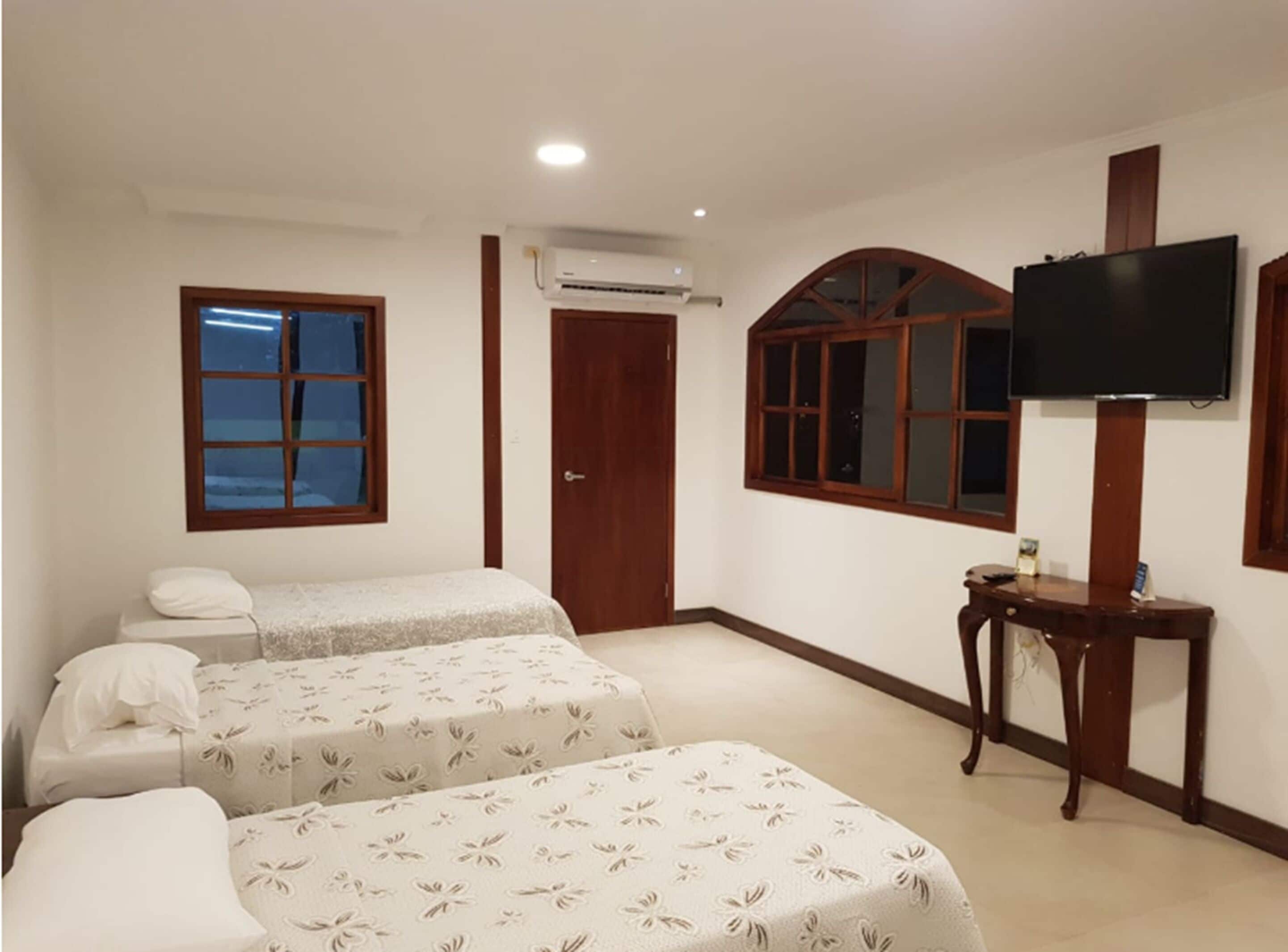 A hotel room with two beds, a TV, and a wooden desk.