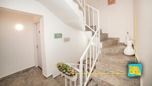A staircase with a white railing, a flower basket, and a yellow measuring tape on the wall. - NİLİA BOZCAADA (Bozcaada)
