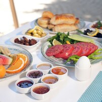 Una mesa con diversos alimentos, como pan, tomates, aceitunas y frutas.