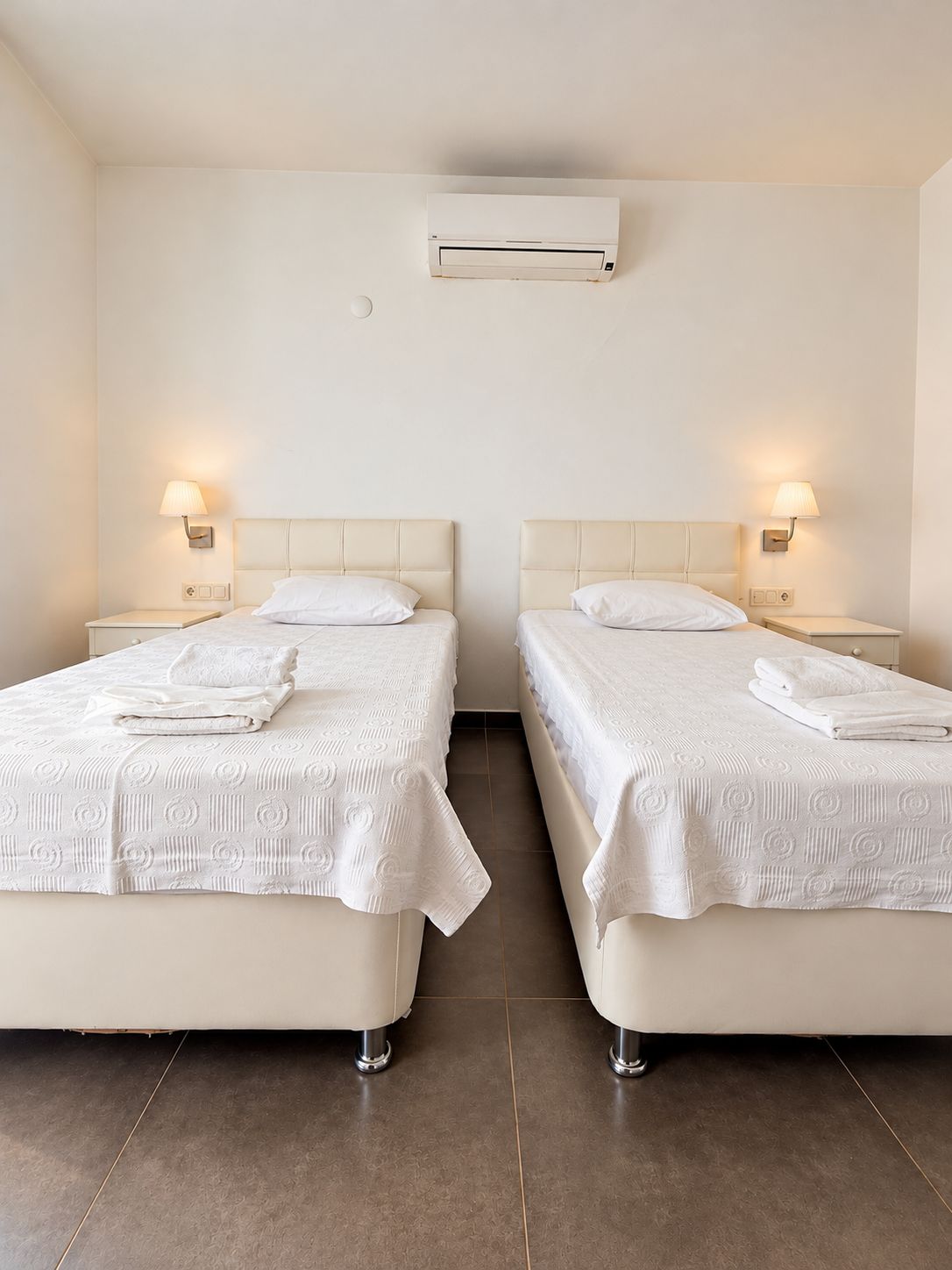 Two twin beds with white bedding and a wall-mounted air conditioner.