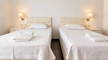 Two twin beds with white bedding and a wall-mounted air conditioner.