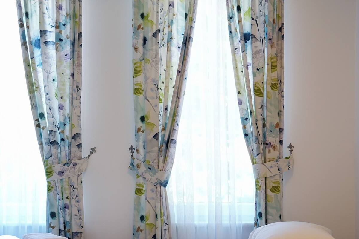 Camera d'albergo con due letti, tende floreali e una parete bianca.