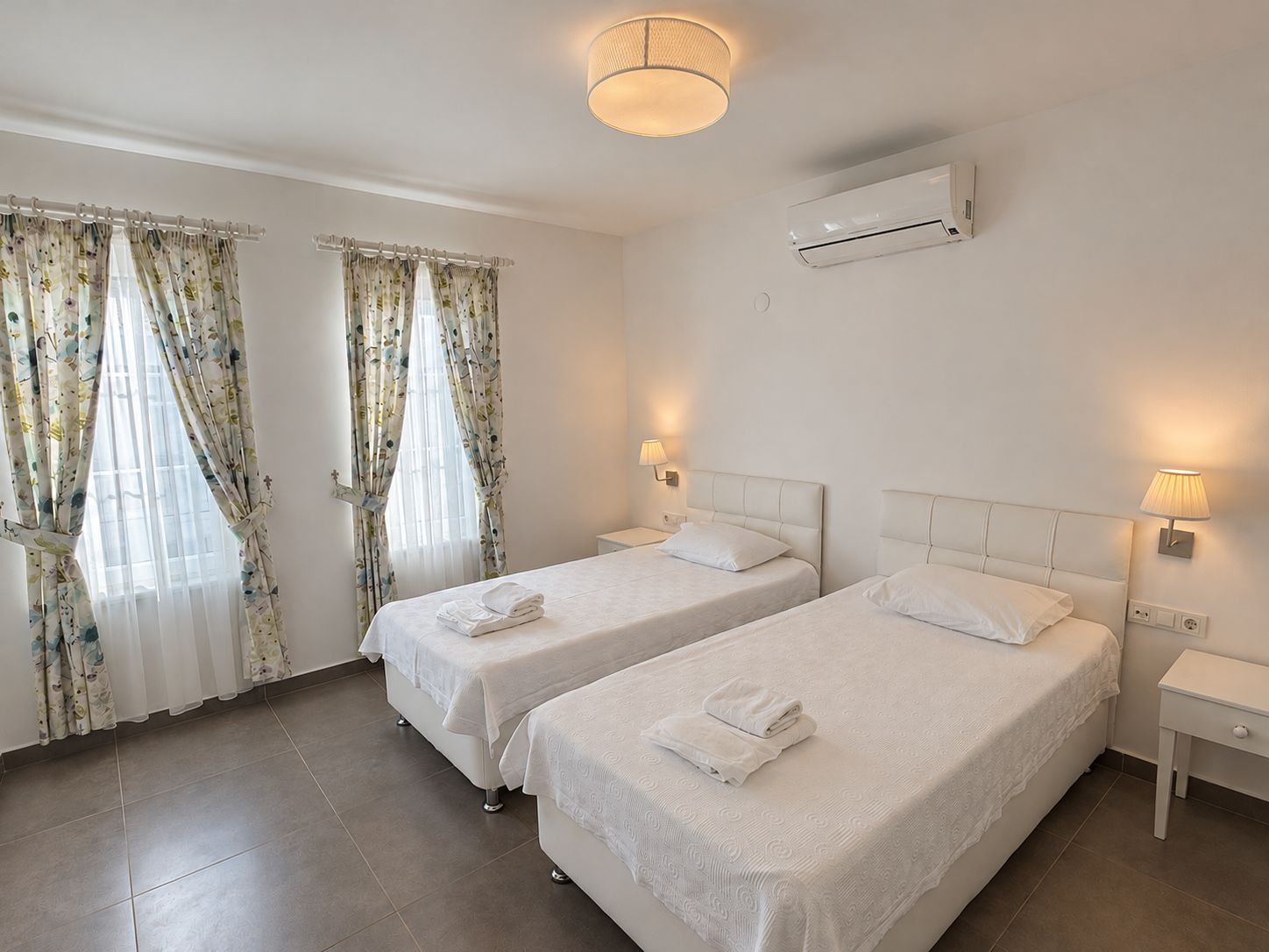 Habitación de hotel con dos camas, una lámpara de techo, un aire acondicionado y cortinas.
