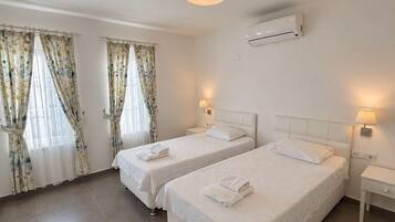 A hotel room with two beds, a ceiling light, an air conditioning unit, and curtains.