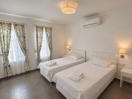 A hotel room with two beds, a ceiling light, an air conditioning unit, and curtains.