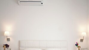 Una habitación de hotel con una cama grande, dos mesitas de noche con lámparas y un equipo de aire acondicionado sobre la cama.