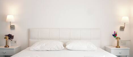 A hotel room with a large bed, two bedside tables with lamps, and an air conditioning unit above the bed.