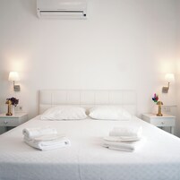 A hotel room with a large bed, two bedside tables with lamps, and an air conditioning unit above the bed.