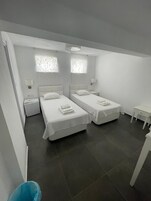 Un dormitorio moderno y minimalista con dos camas, una mesita pequeña y una silla.
