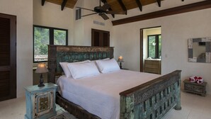 Une chambre à coucher avec un lit en bois, un ventilateur de plafond et une vue sur l’extérieur par une fenêtre.