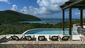 Un espace aménagé au bord de la piscine, avec des chaises longues, une terrasse dallée de pierre et une vue sur l’océan et les îles lointaines.