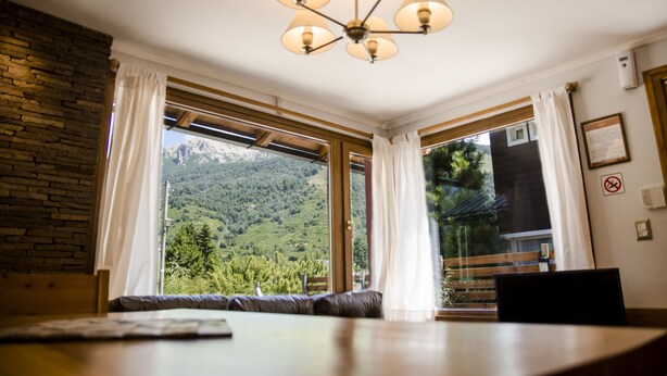 Una stanza con un'ampia finestra vista sulle montagne, un soffitto in legno e un lampadario.