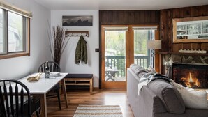 A cozy living room with a fireplace, a dining area with a bench, and a view of the outdoors through a sliding door. - Outpost: Spruces 10 - Located in the Aspens! (Wilson)