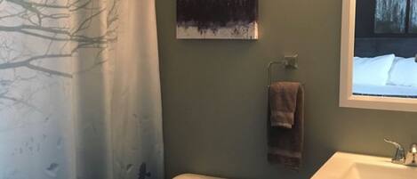 A bathroom with a toilet, a sink, a mirror, a painting of trees, and a shower curtain.
