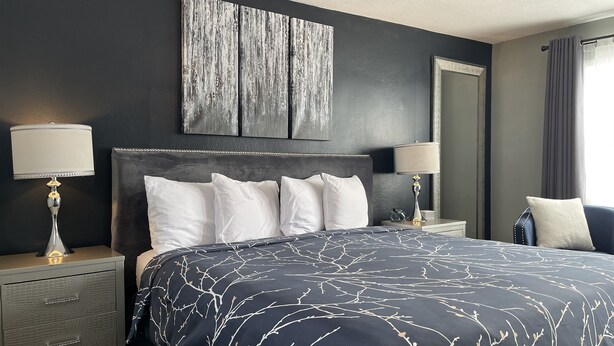A modern hotel room with a large bed, two bedside tables, a nightstand, a mirror, and a window with curtains.
