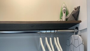 A kitchen with a wooden shelf holding a green and white appliance, a patterned pot hanging, and white hangers for kitchen utensils.