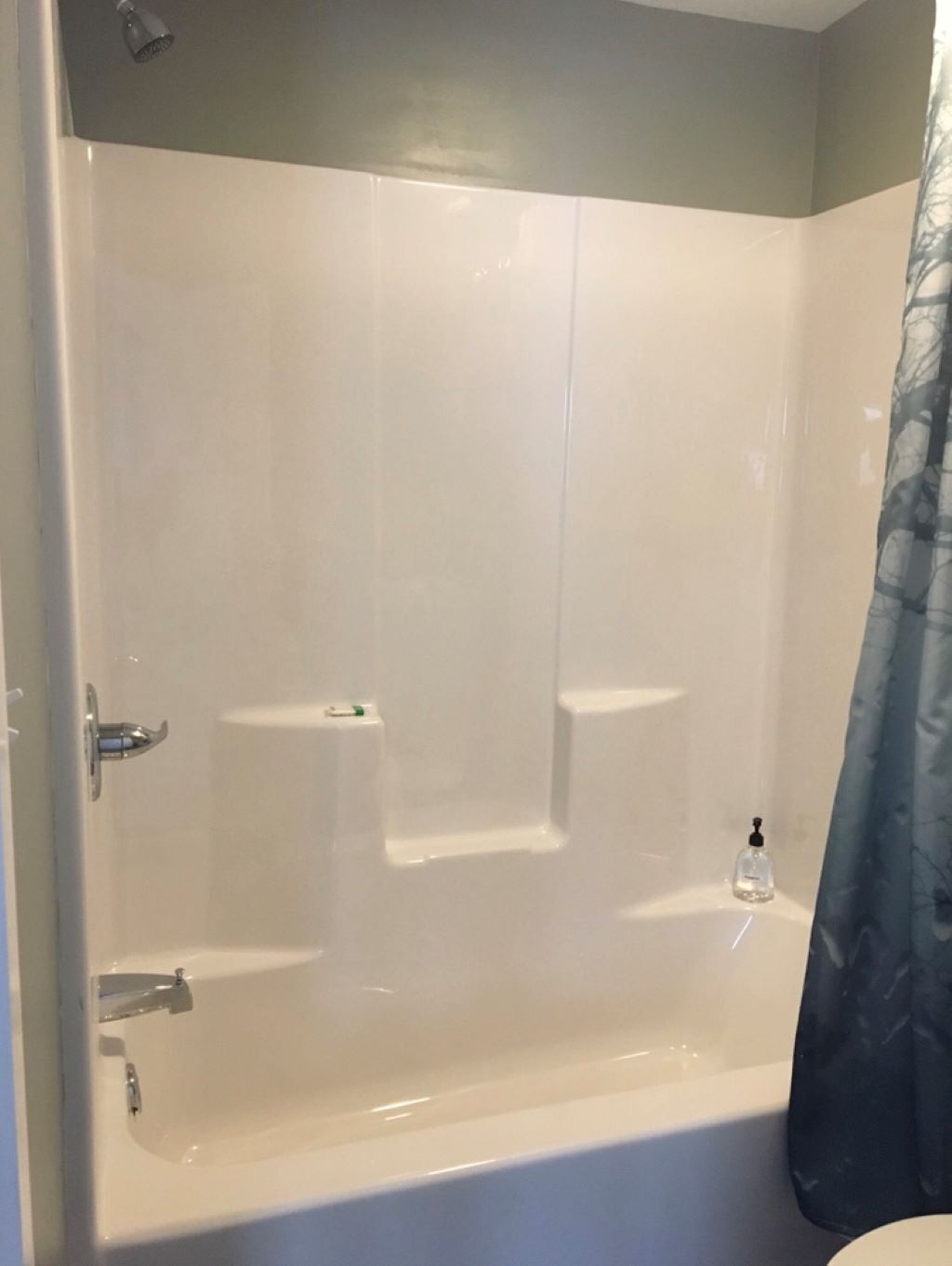 A white bathtub with a showerhead above it, a soap dispenser, and a curtain partially visible.