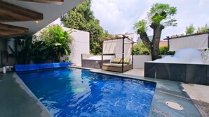 A swimming pool with a blue water feature, surrounded by a modern outdoor seating area with a cushioned bench and a small table. - Style & Design Loft: 2 PRIVATE JACUZZIS, POOL, TERRACE, GRILL! (Cuernavaca)