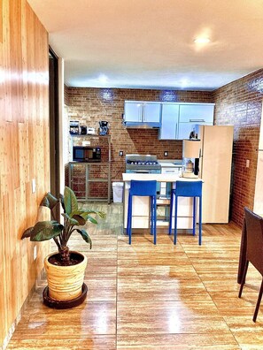 A modern kitchen with a brick wall, white cabinets, and a dining area with blue chairs. - Style & Design Loft: 2 PRIVATE JACUZZIS, POOL, TERRACE, GRILL! (Cuernavaca)