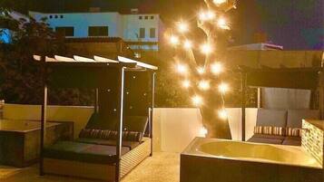 Une terrasse sur le toit avec un espace salon couvert, un jacuzzi et des guirlandes lumineuses.