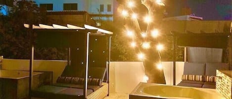 A rooftop terrace with a covered seating area, a hot tub, and string lights.