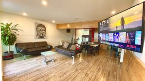A modern living room with a large flat-screen TV displaying a movie selection, a sofa set, a coffee table, and a potted plant. - Style & Design Loft: 2 PRIVATE JACUZZIS, POOL, TERRACE, GRILL! (Cuernavaca)
