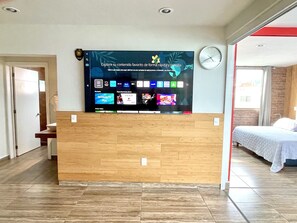 A hotel reception area with a large digital screen displaying various content options, a clock, and a bed in the adjacent room. - Style & Design Loft: 2 PRIVATE JACUZZIS, POOL, TERRACE, GRILL! (Cuernavaca)
