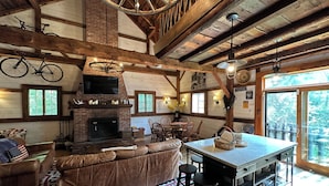 A rustic interior with a fireplace, wooden beams, a dining area, and a kitchen with bar stools. - One of a kind cozy Renovated VT Barn- where Family, Friends, Couples gather  (Shaftsbury)