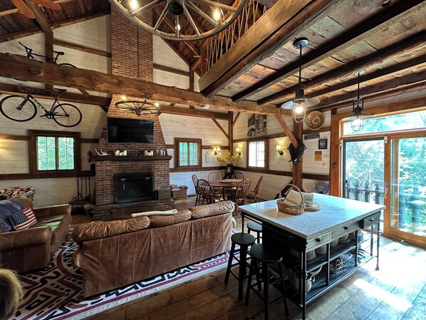 A rustic interior with a fireplace, wooden beams, a dining area, and a kitchen with bar stools.