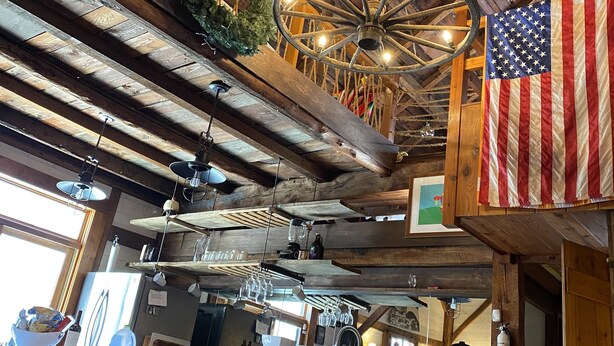 A rustic interior with exposed wooden beams, a hanging light fixture, and an American flag. - One of a kind cozy Renovated VT Barn- where Family, Friends, Couples gather  (Shaftsbury)