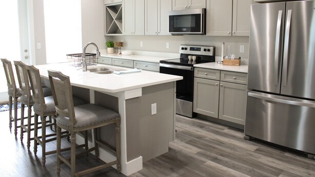 A modern kitchen with a central island, stainless steel appliances, and a dining area with wooden chairs.