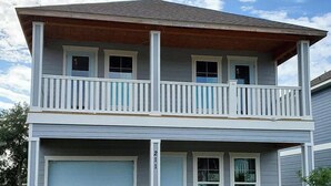 A two-story house with a front garage, a balcony on the upper floor, and a brick driveway.