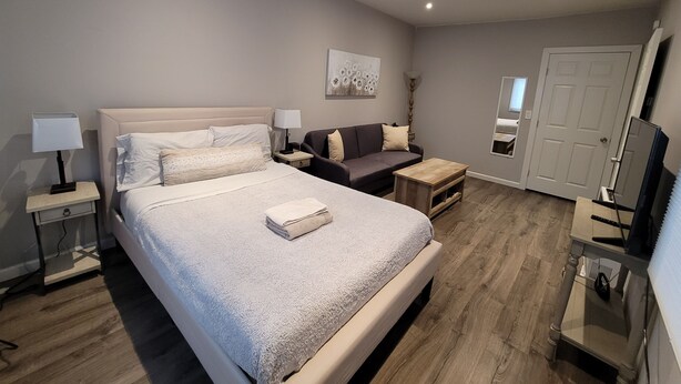 A modern hotel room with a large bed, a sofa, a small table, and a TV. - Remodeled Cottage in Trendy Berkeley/Oakland Rockridge Area (Oakland)