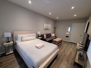 A modern hotel room with a large bed, a sofa, a small table, and a TV.
