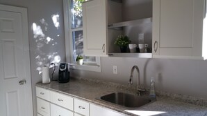 A modern kitchen with white cabinets, a stainless steel sink, a coffee maker, and a small potted plant on the windowsill. - Remodeled Cottage in Trendy Berkeley/Oakland Rockridge Area (Oakland)