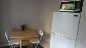 A compact kitchen with a microwave on top of a white refrigerator, a small wooden table, two white chairs, and a potted plant. - Remodeled Cottage in Trendy Berkeley/Oakland Rockridge Area (Oakland)