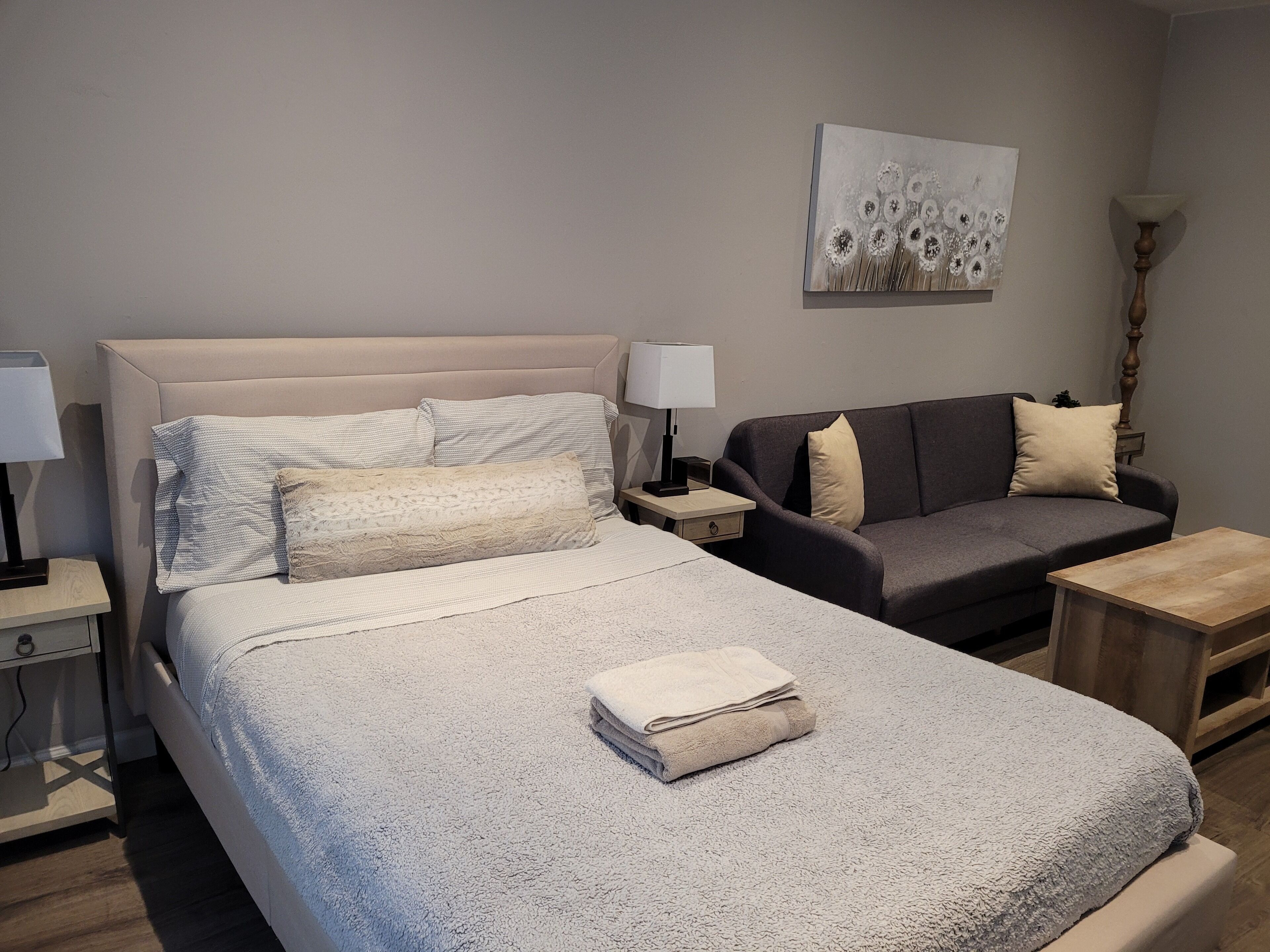 A hotel room with a bed, a sofa, a nightstand with a lamp, and a painting on the wall.