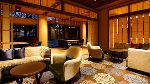Un hall d’entrée spacieux avec un plafond haut, de poutres en bois traditionnelles et de grandes portes coulissantes. Le mobilier comprend des canapés, des fauteuils et une petite table ronde.
