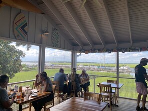 A covered outdoor seating area with tables and chairs, overlooking a body of water and farmland. - Sweet cottage, Best Location, Close to Everything, River View (Beaufort)