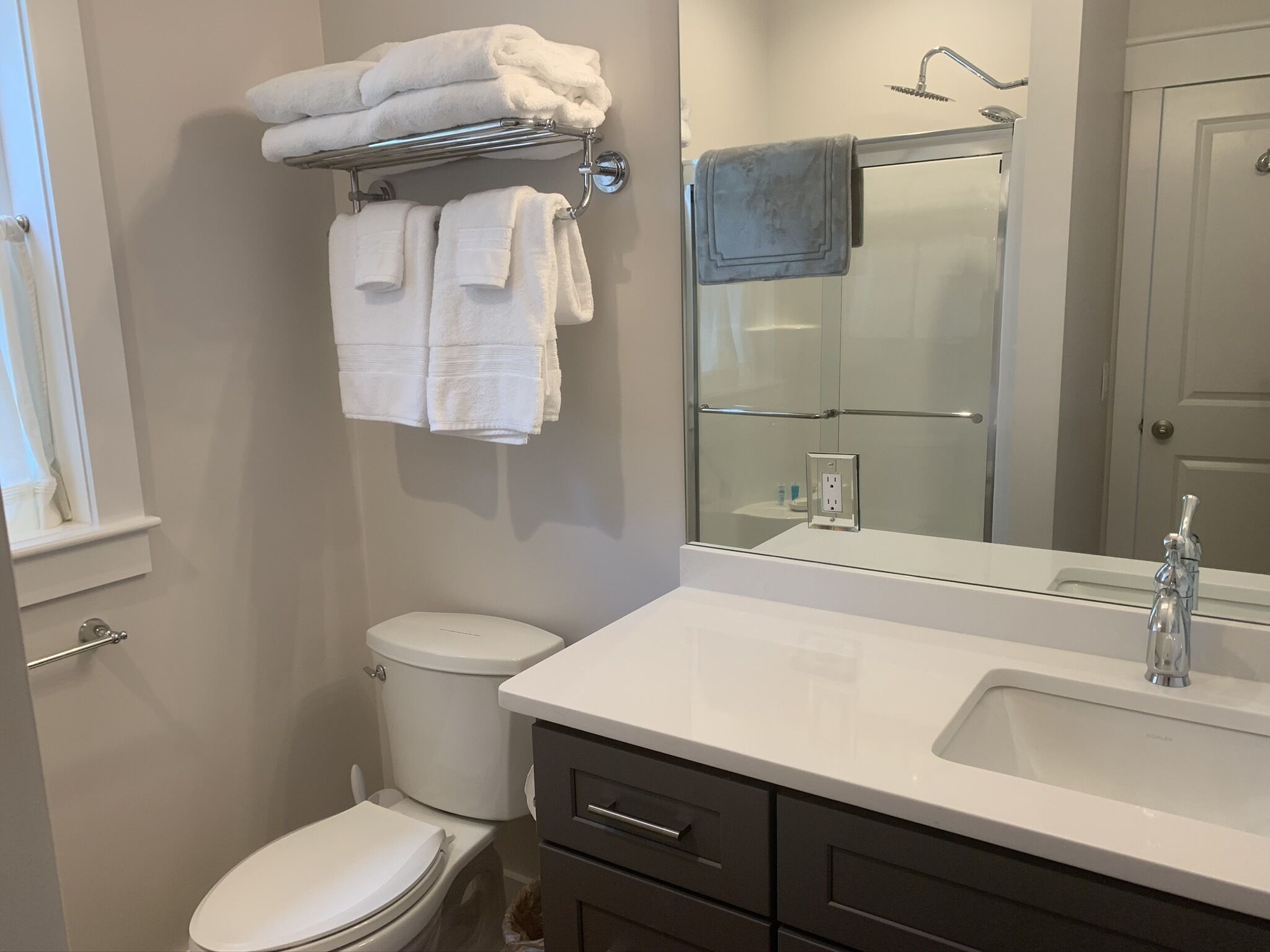 Een badkamer met een toilet, een wastafel, een spiegel en een handdoekrek met opgevouwen handdoeken.