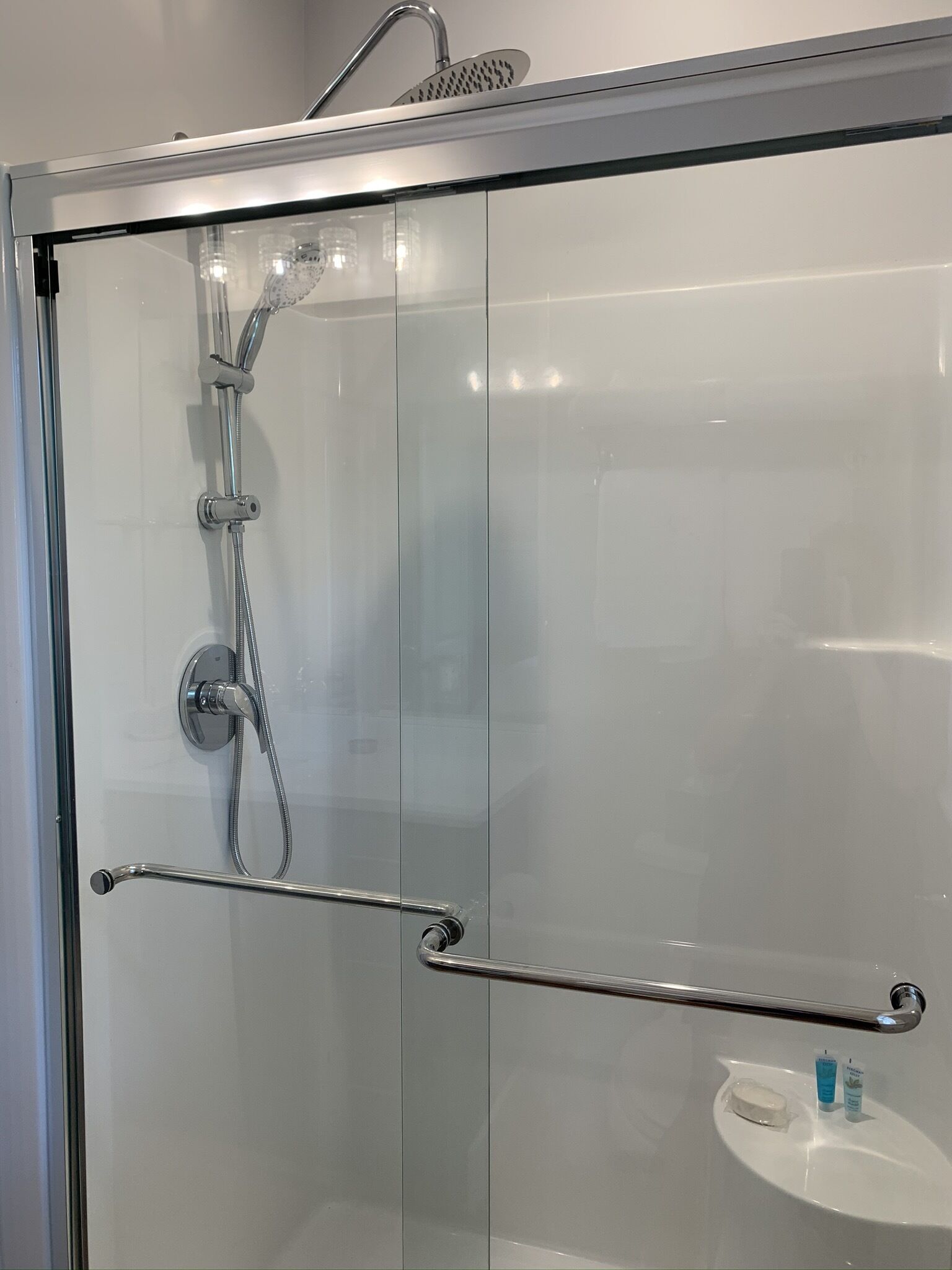 A modern shower enclosure with a glass door, a handheld showerhead, and a handheld shower attachment.
